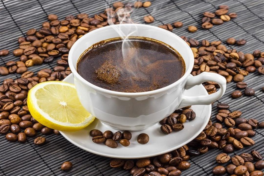 فنجان قهوة بجانب شرائح الليمون على طاولة خشبية