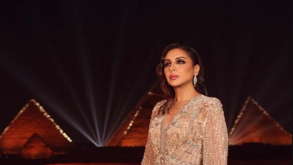 الفنانة أنغام بإطلالة ساحرة بفستان طويل مطرز بالكامل أثناء حفلها عند سفح الأهرامات، مع مكياج ناعم وشعر منسدل.