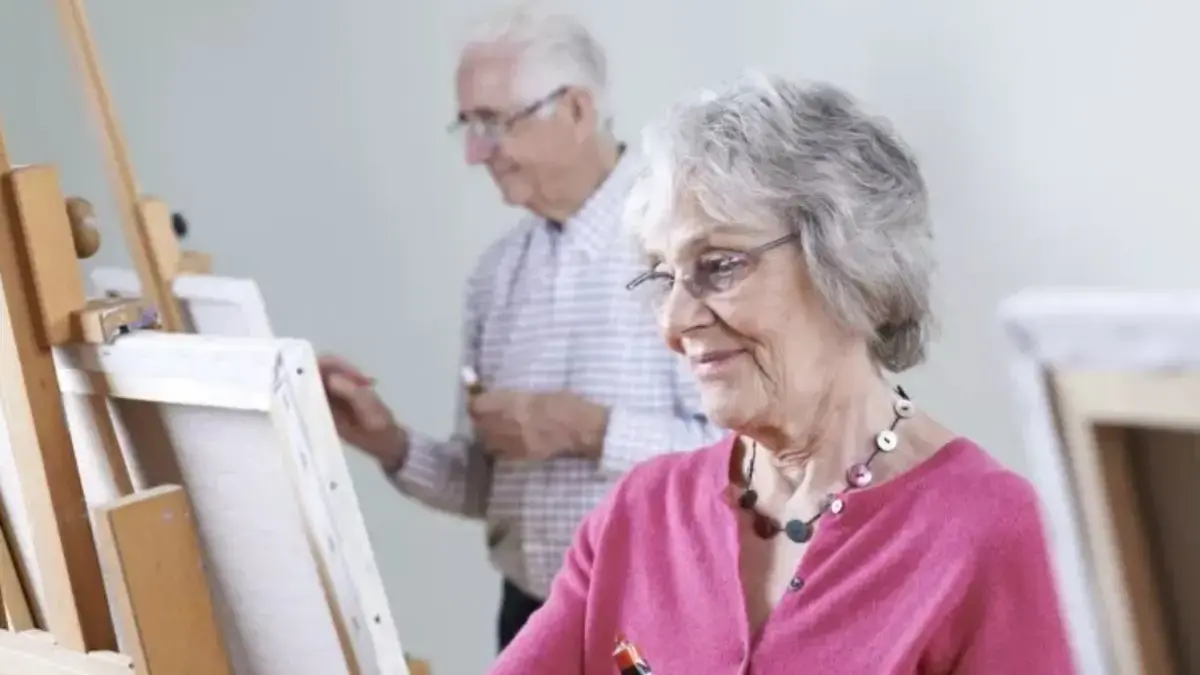 شخص مسن يعزف على آلة موسيقية وسط ألوان وأدوات فنية، مما يعكس نشاطات إبداعية للحفاظ على صحة الدماغ