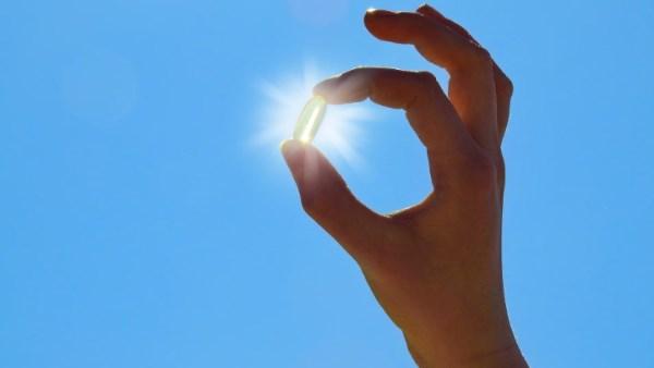 علبة مكملات فيتامين D إلى جانب أطعمة غنية بالفيتامين وأشعة الشمس