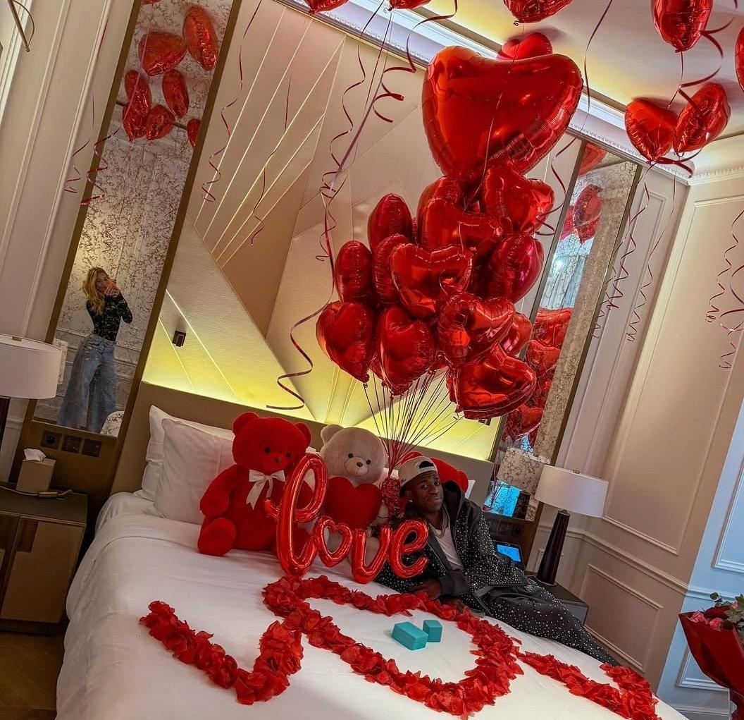 فينيسيوس جونيور يطلب يد فيرجينيا فونسيكا داخل غرفة مزينة بالبالونات والورود الحمراء في أجواء رومانسية.